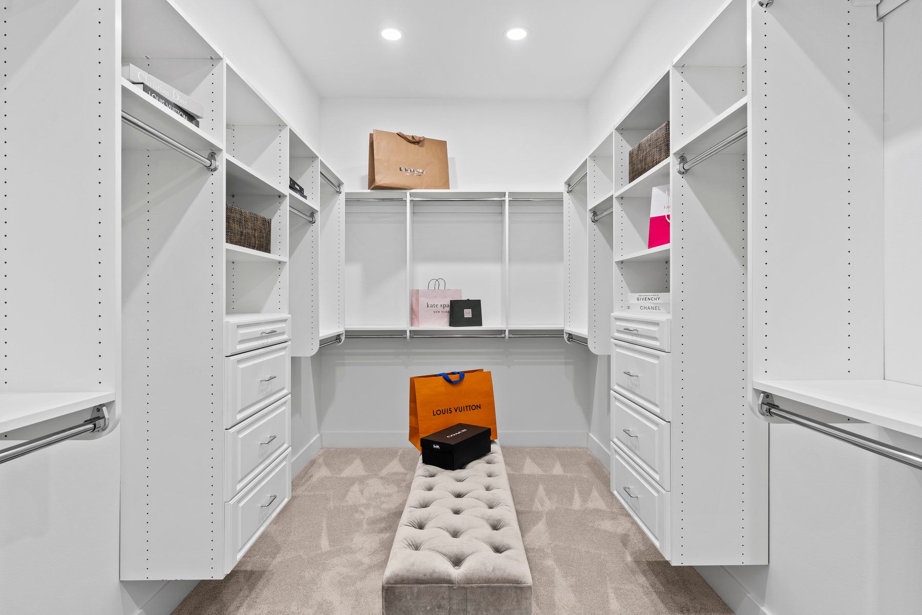 A walk in closet with lots of shelves and drawers and a bench.