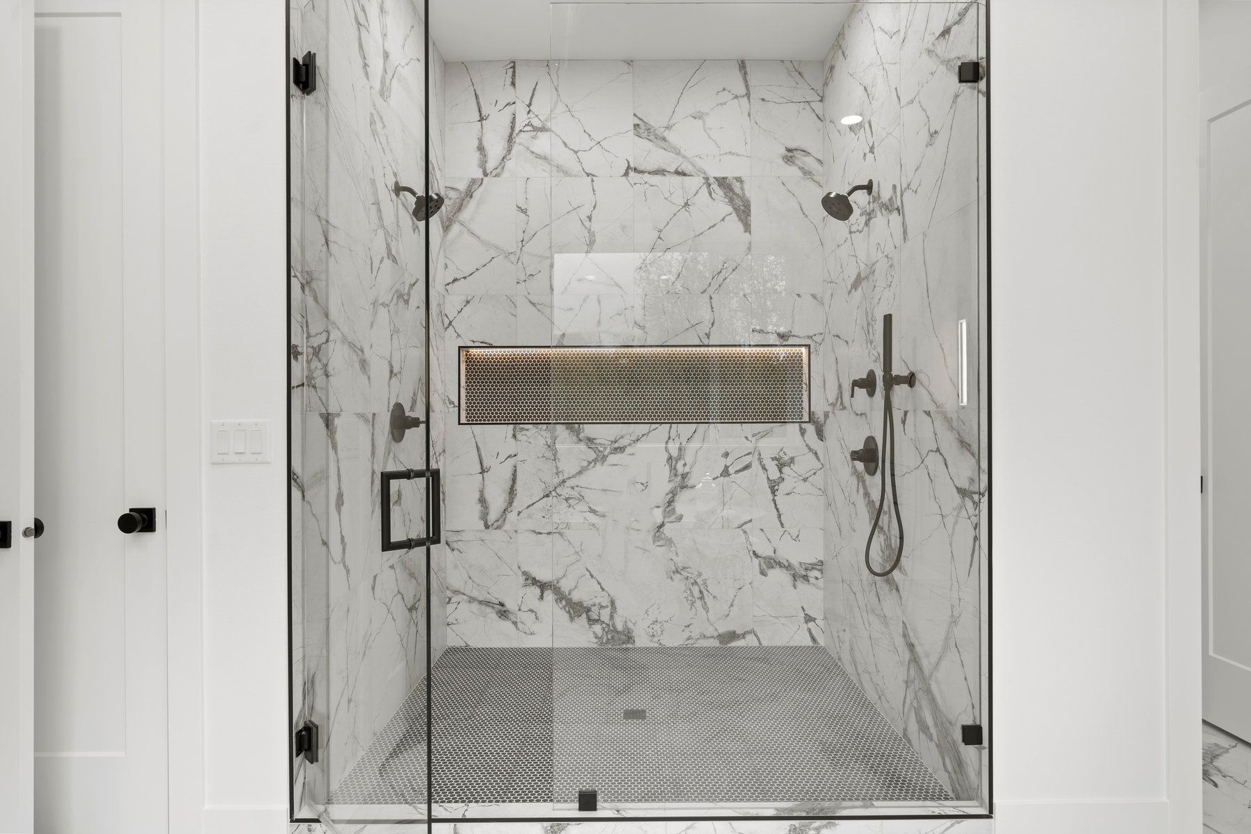 A bathroom with marble walls and a walk in shower with a glass door.