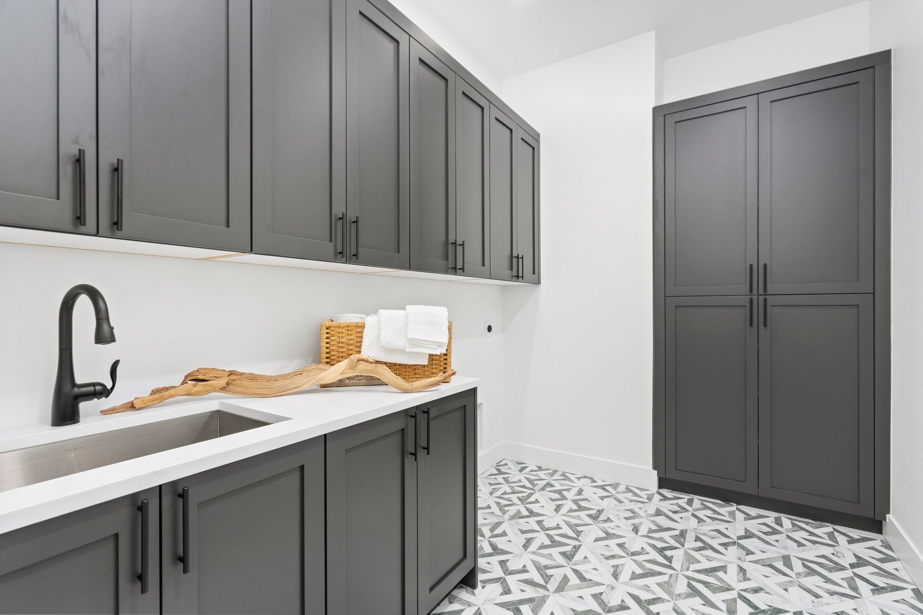 A laundry room with gray cabinets and a sink.