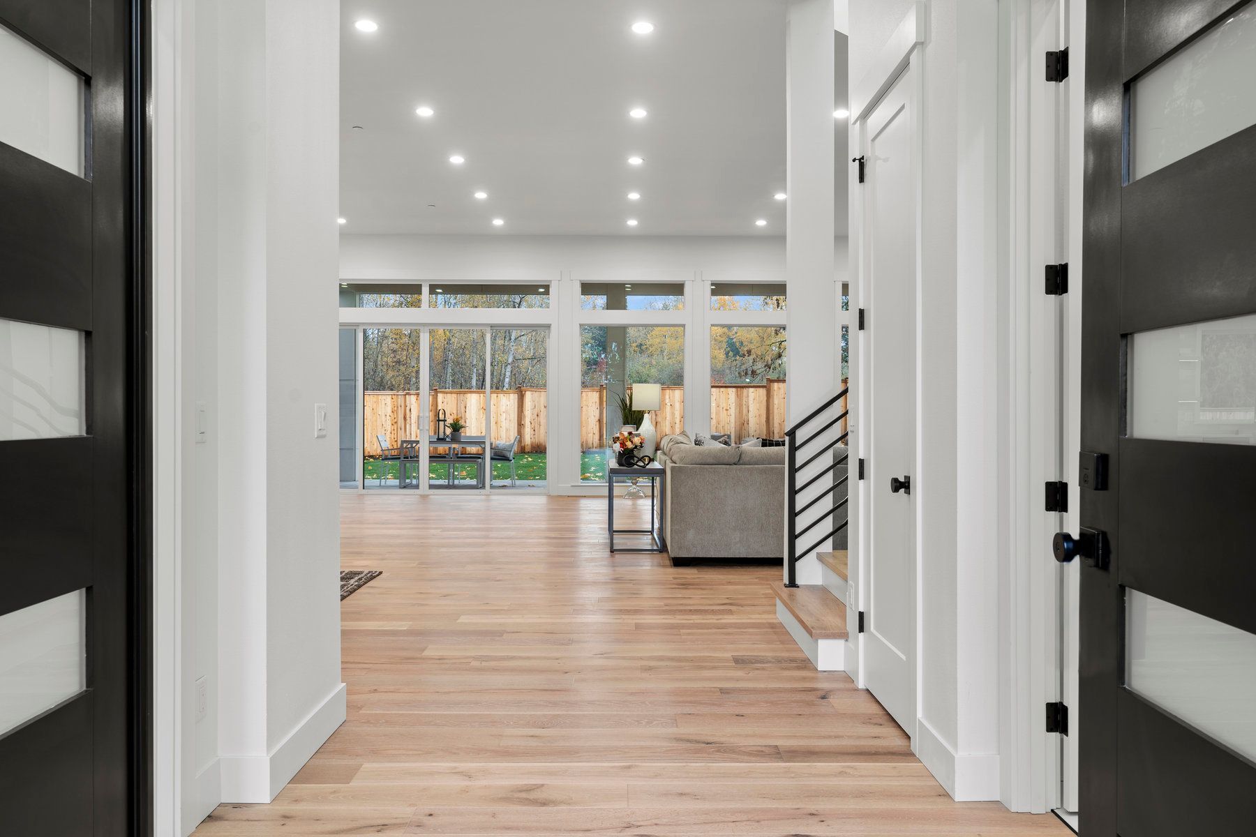 A hallway in a house with hardwood floors and black doors leading to a living room.
