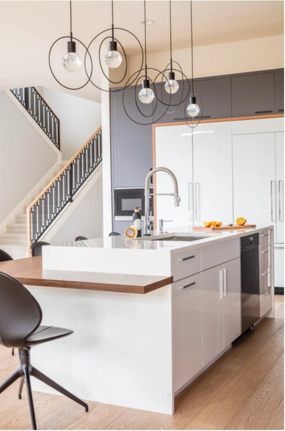 A kitchen with a large island , sink , refrigerator and stairs.