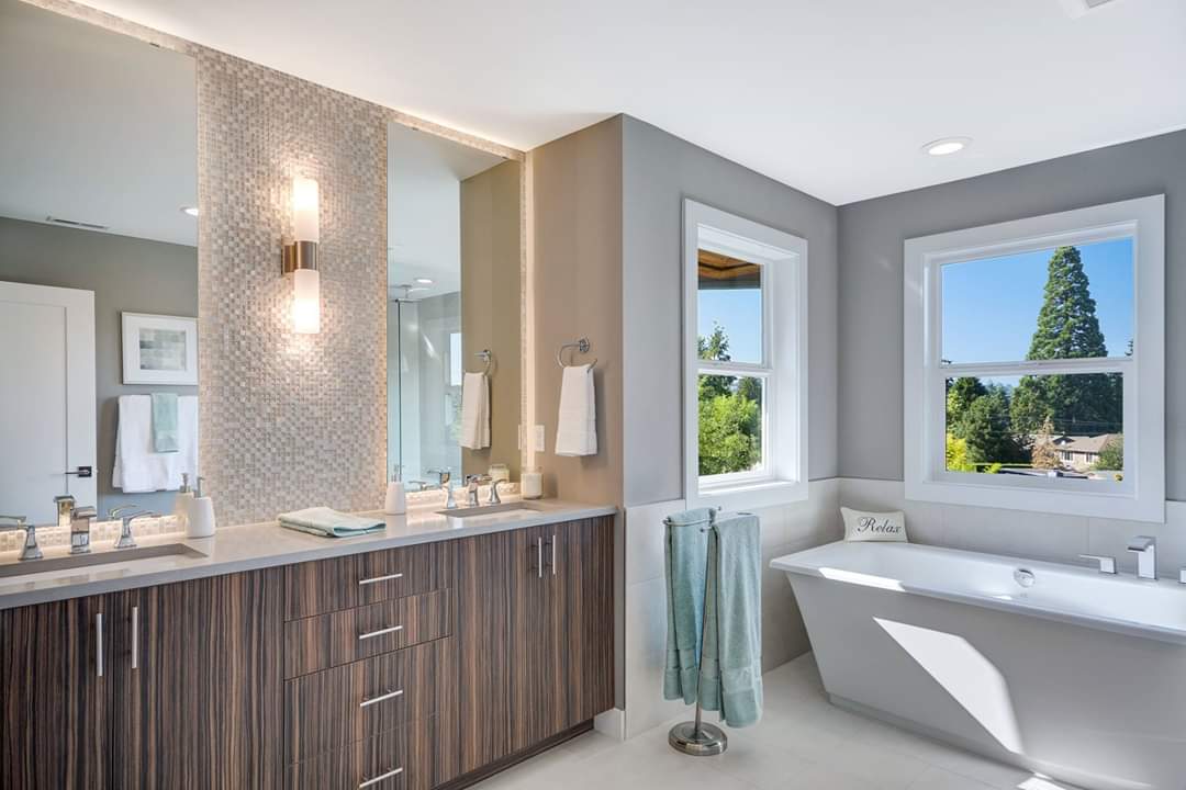 A bathroom with a tub , sink , mirror and window.