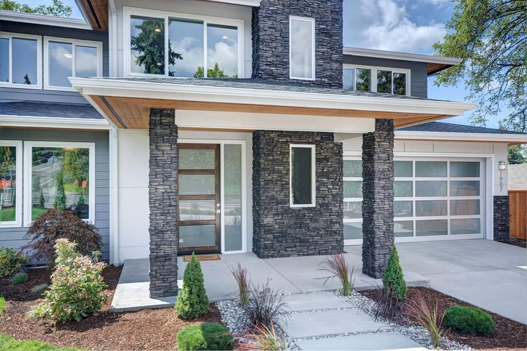 A modern house with a stone facade and a glass garage door.