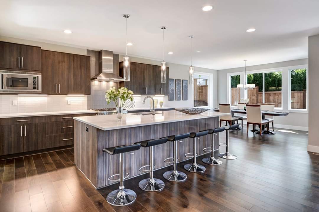A kitchen with a large island and stools and a dining room in the background.