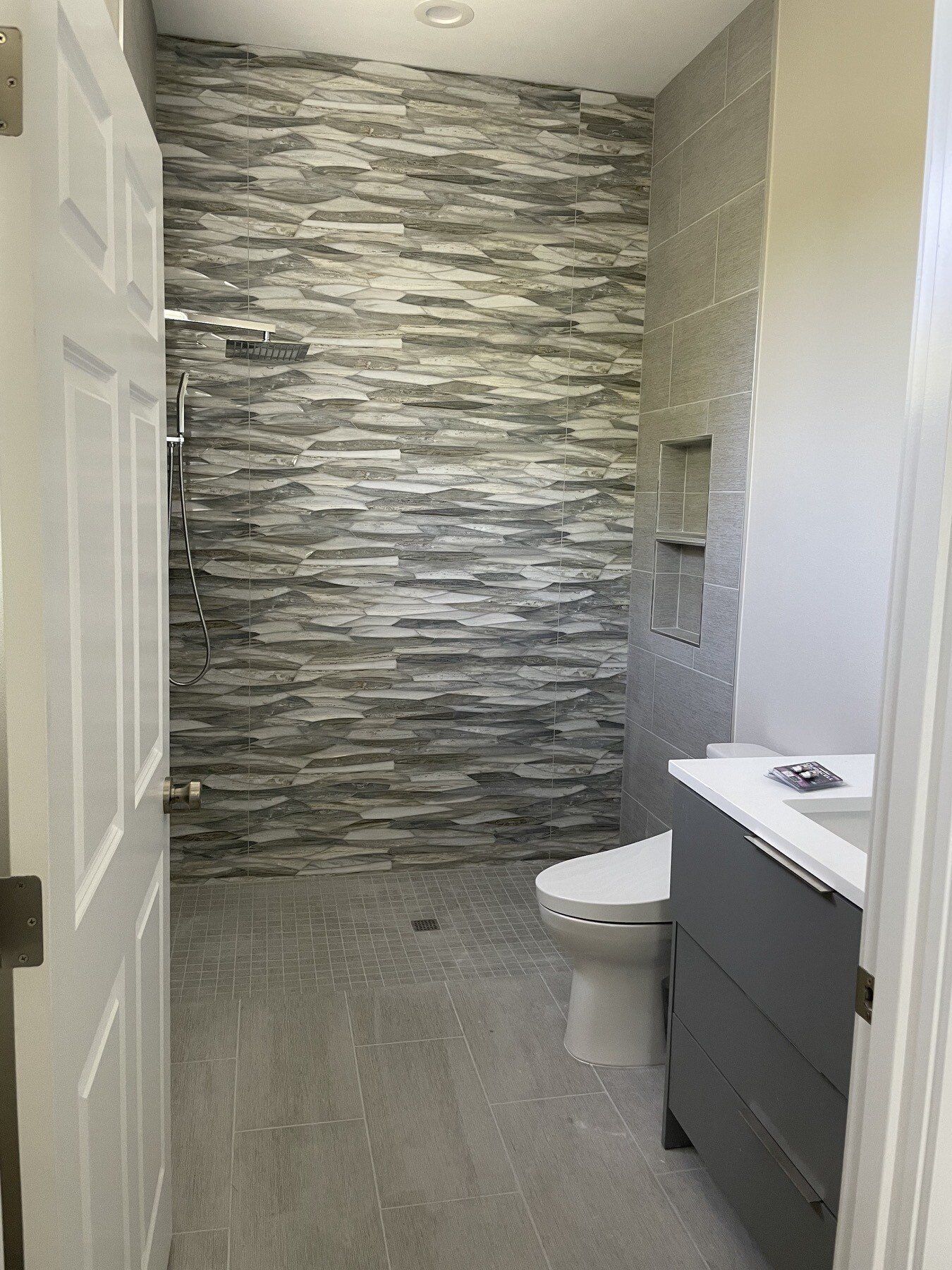 A bathroom with a toilet , sink and shower with a stone wall.