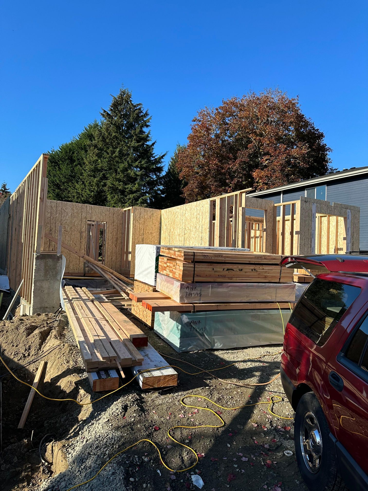 A red car is parked in front of a building under construction.