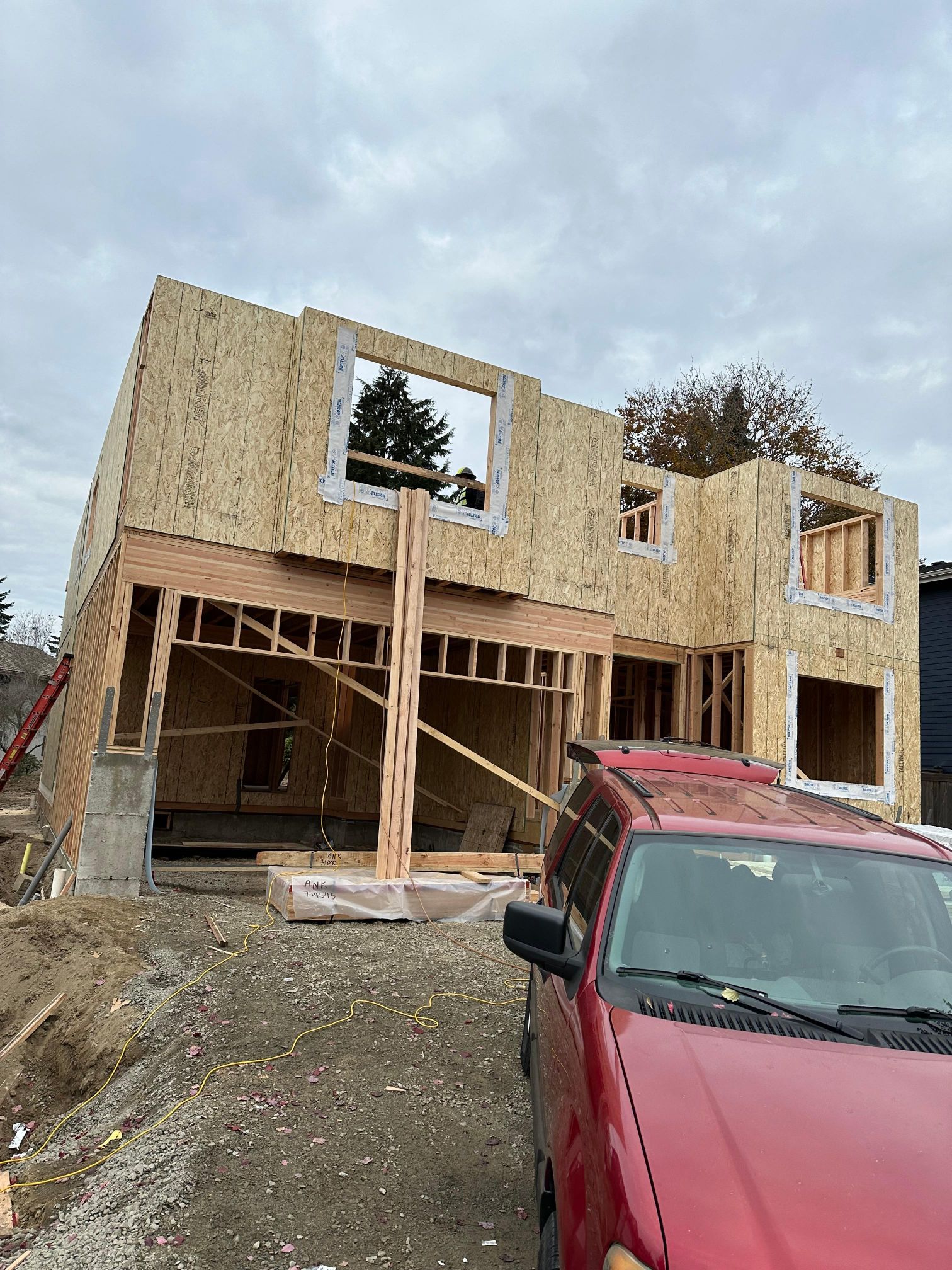 A red car is parked in front of a house under construction.