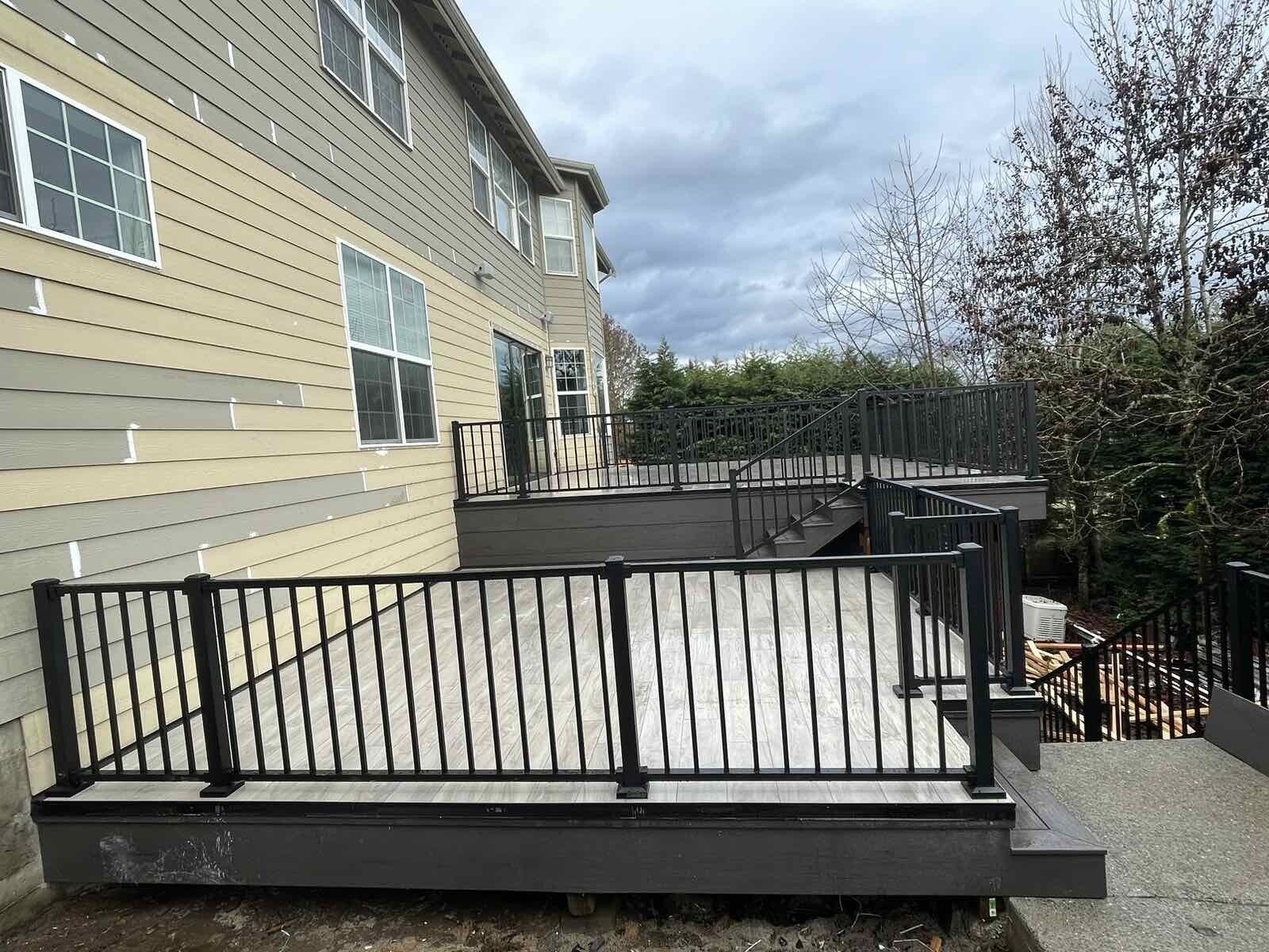 A large deck with a black railing is in front of a house.