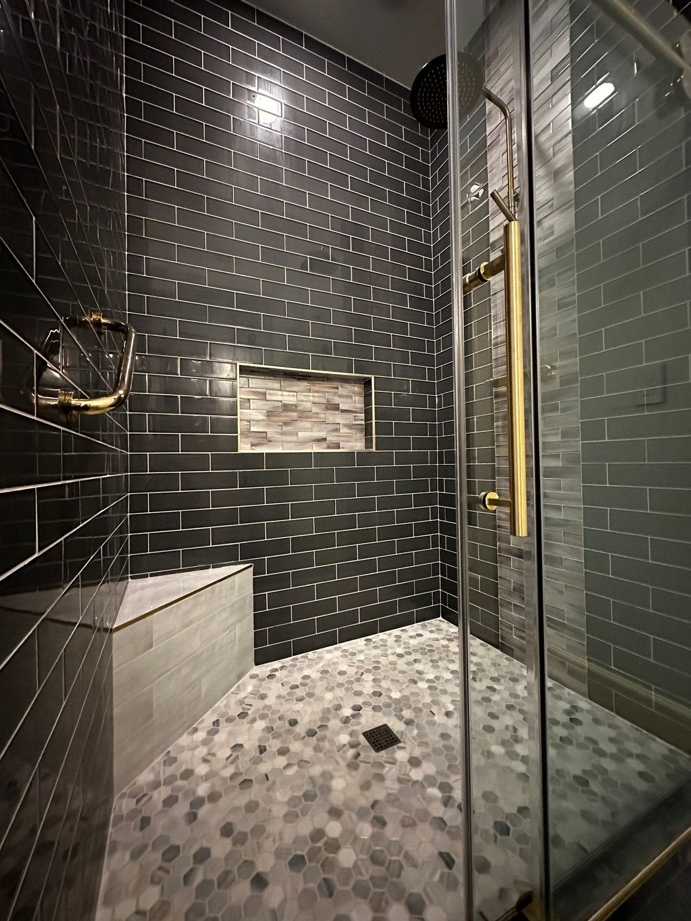 A walk in shower with black tiles and a glass door.