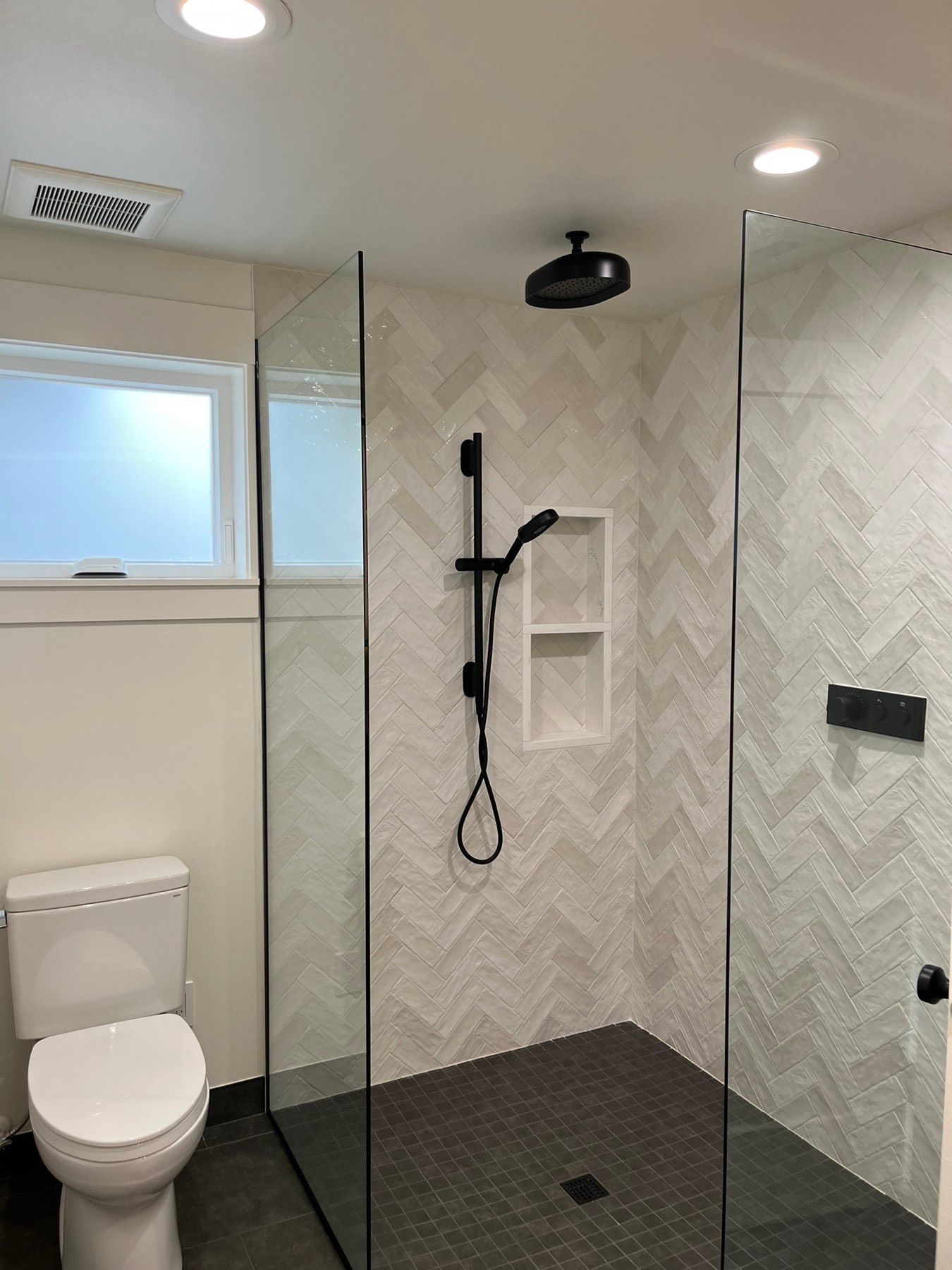 A bathroom with a toilet , shower , and window.