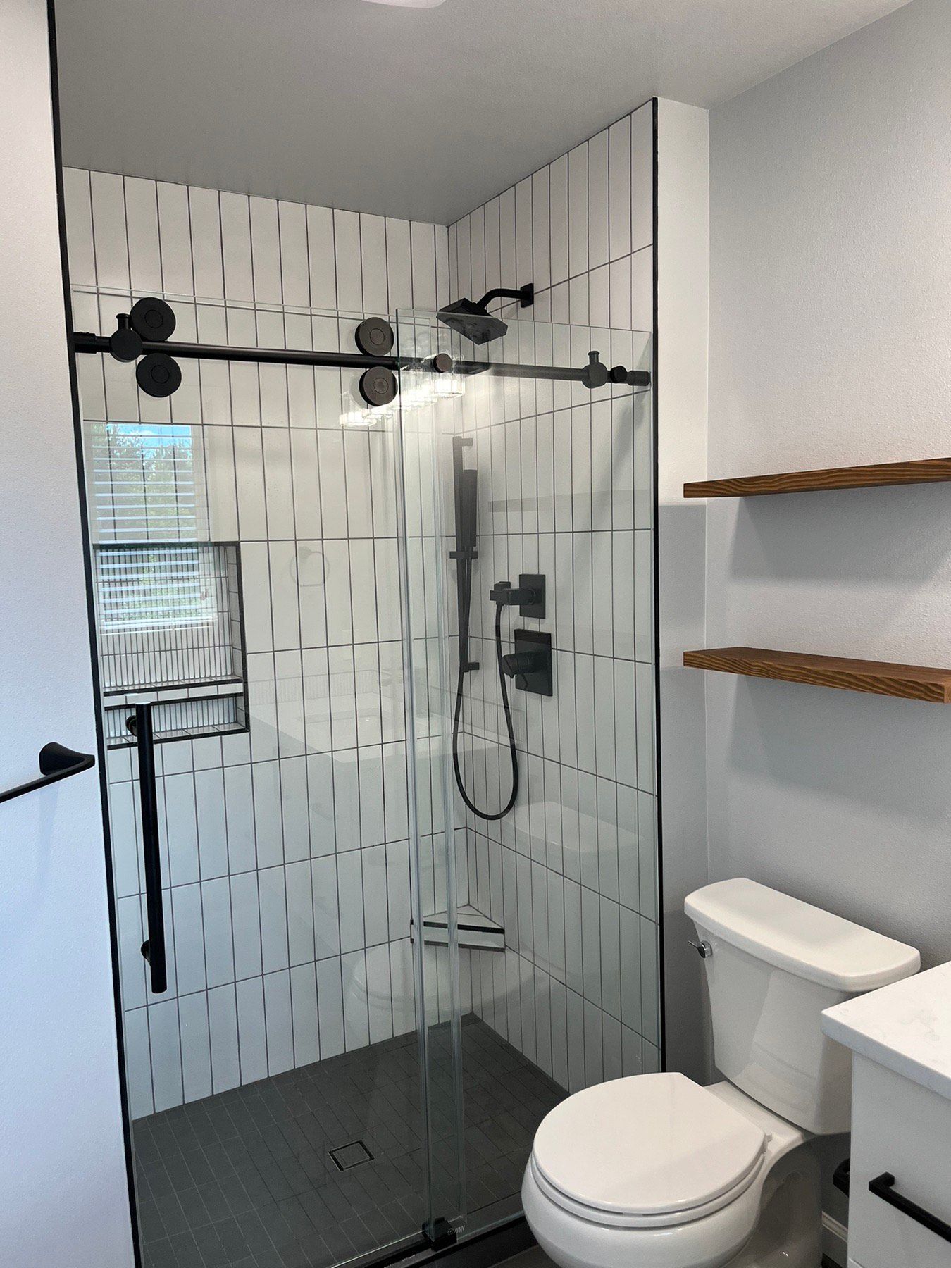 A bathroom with a toilet , shower , and shelves.