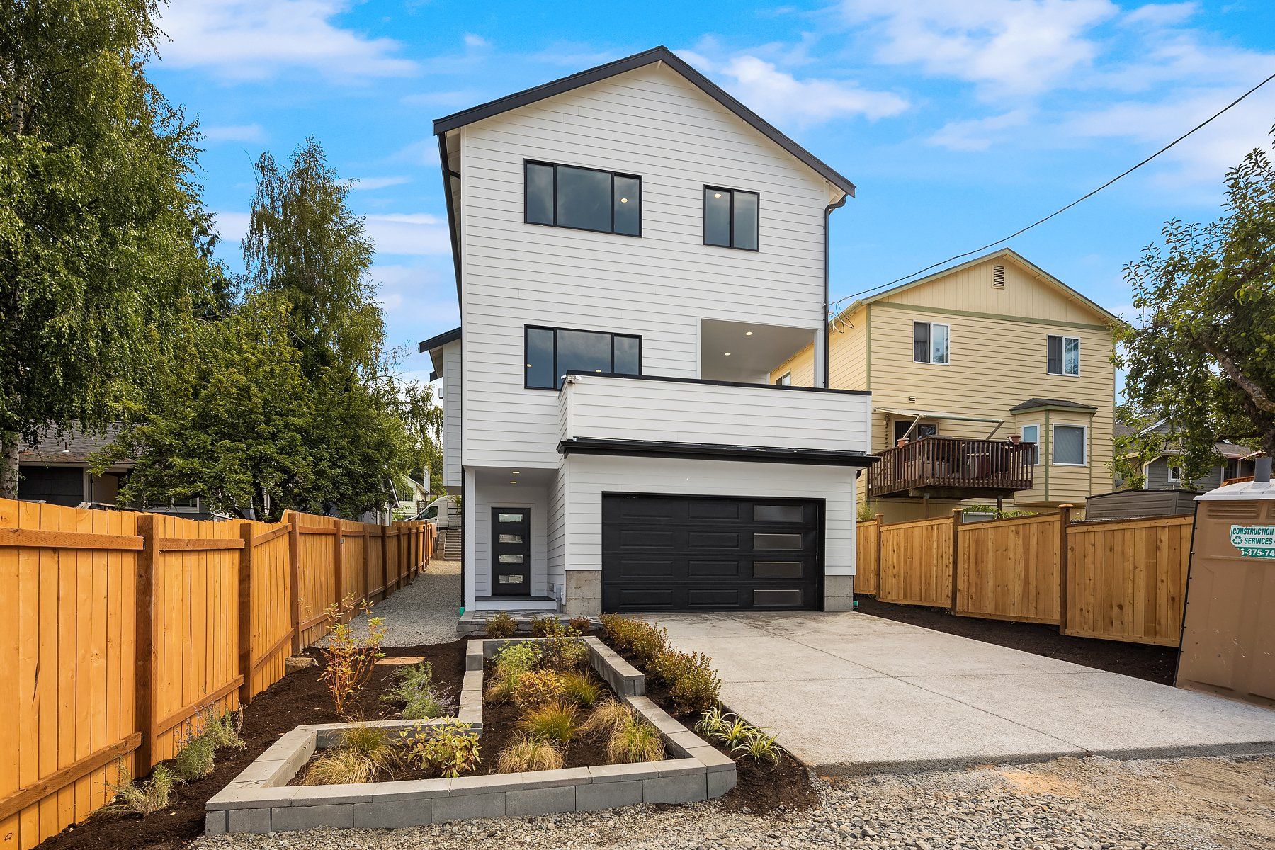 A white house with a black garage door is surrounded by a wooden fence.