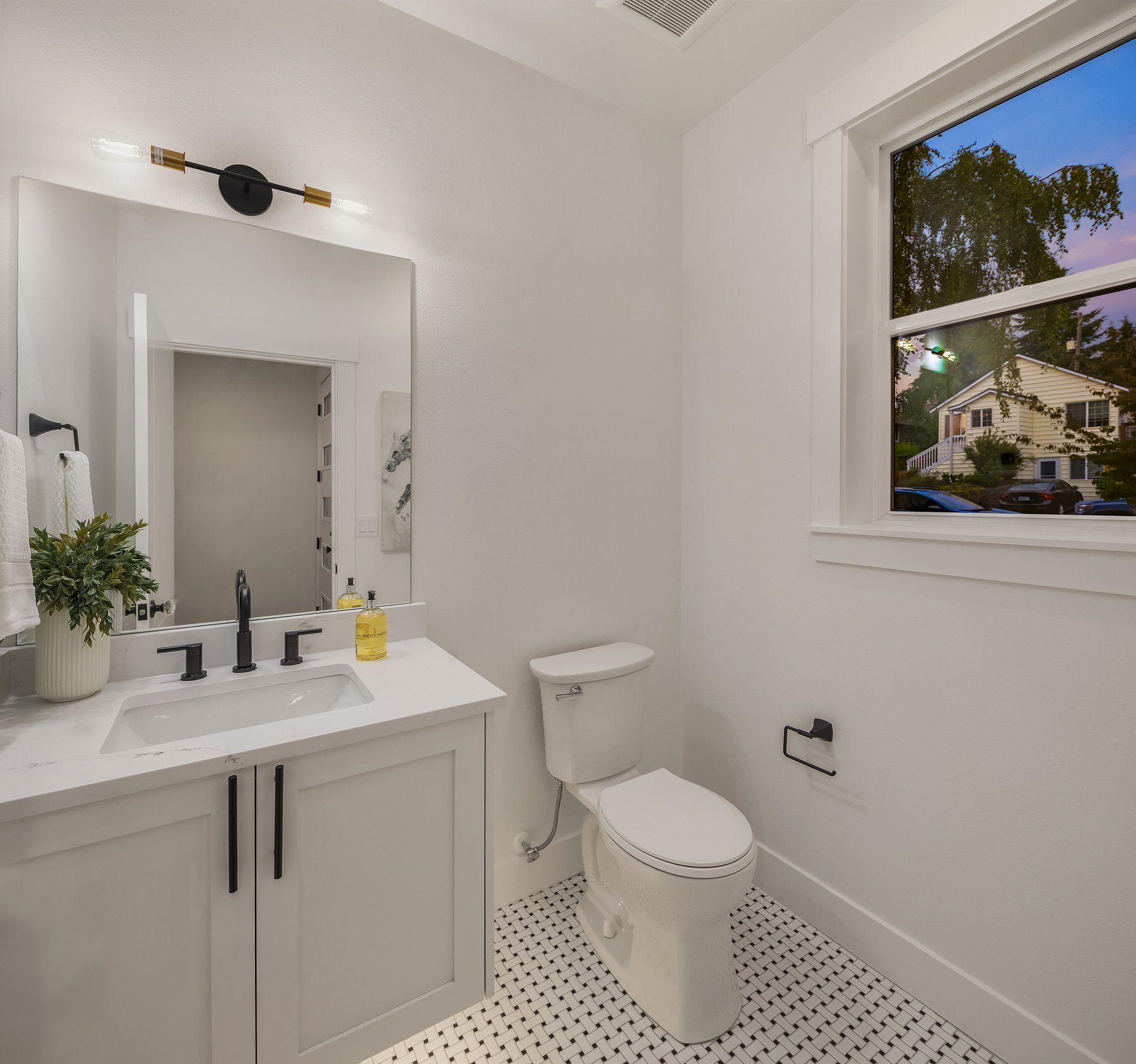 A bathroom with a sink , toilet , mirror and window.