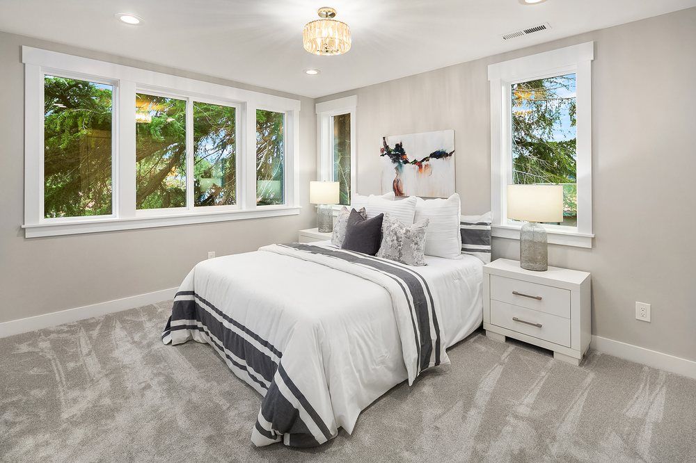 A bedroom with a bed , nightstands , lamps and windows.
