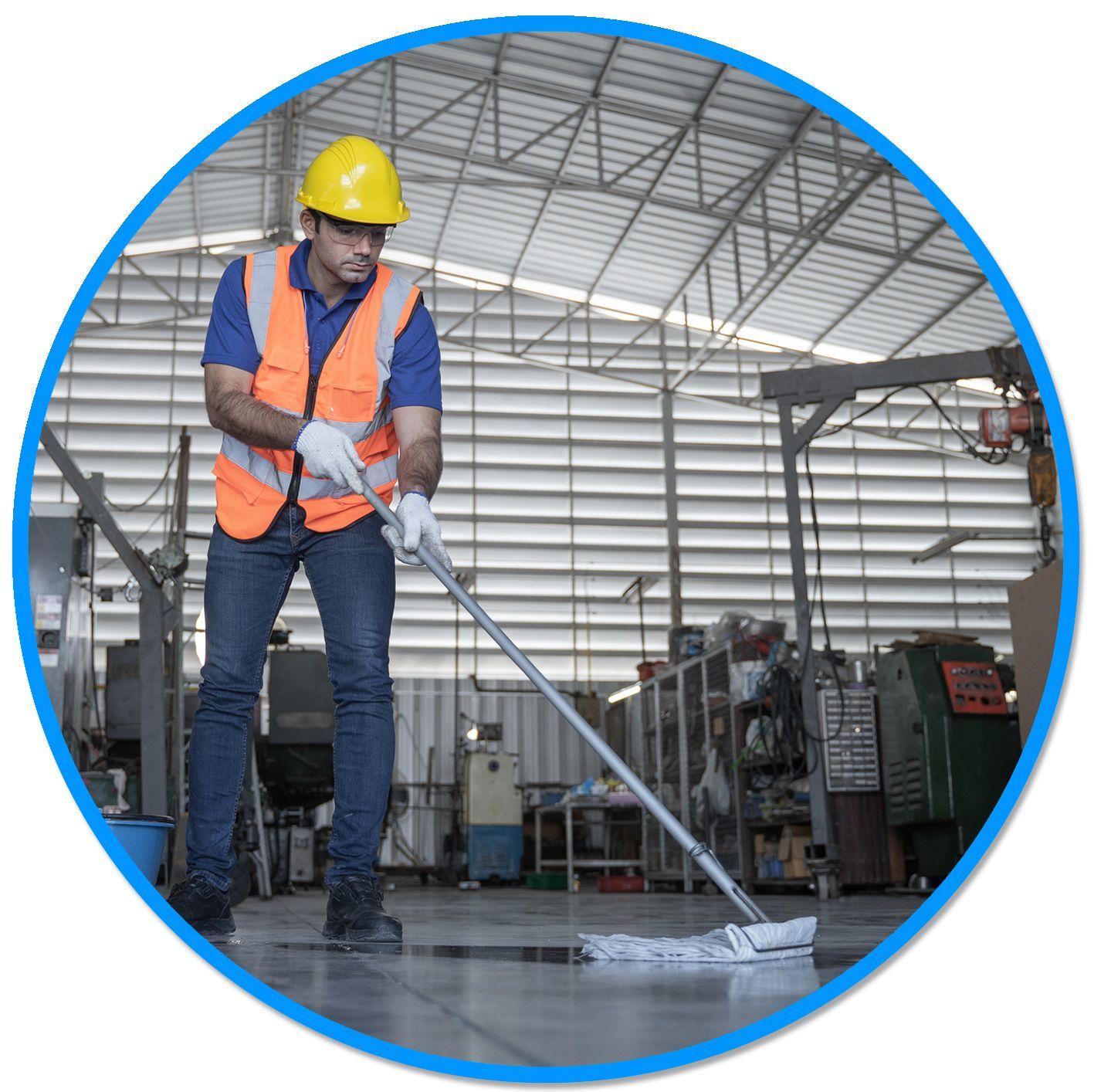 A man wearing a hard hat is mopping the floor in a warehouse.