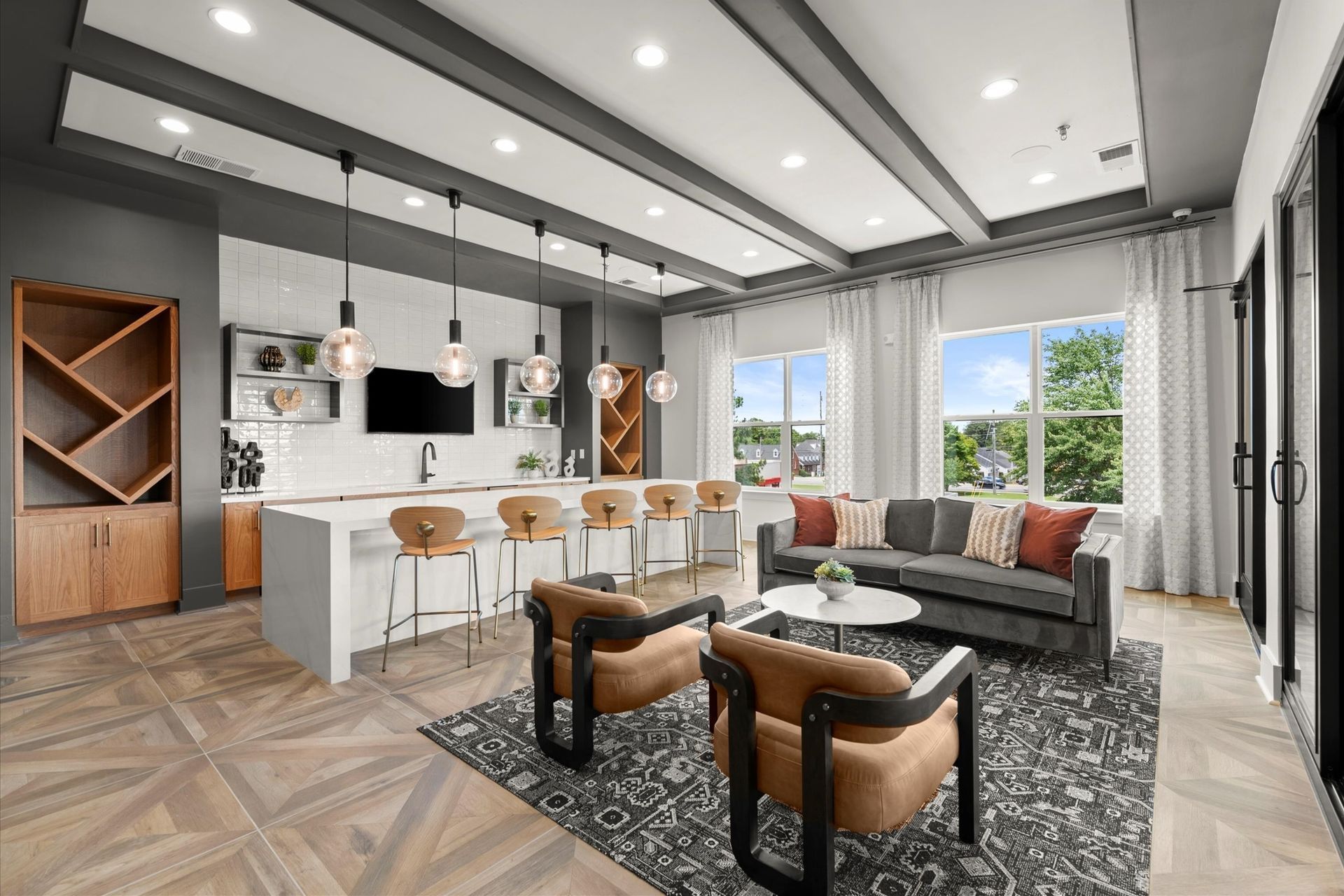 Modern apartment lounge with kitchen, seating area, and large windows; neutral colors, pendant lights.