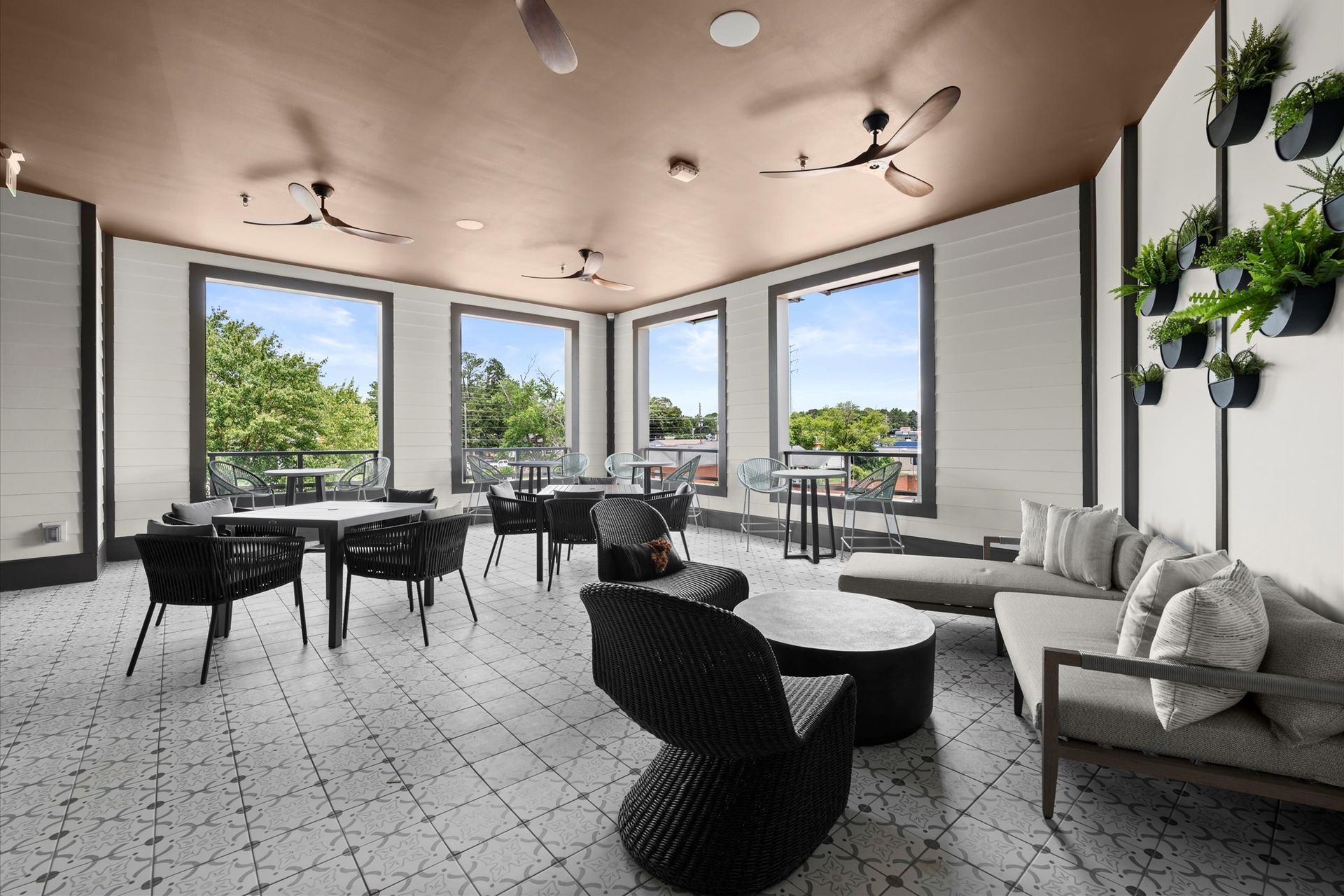 Indoor lounge with tables, seating, windows, and plants on walls.