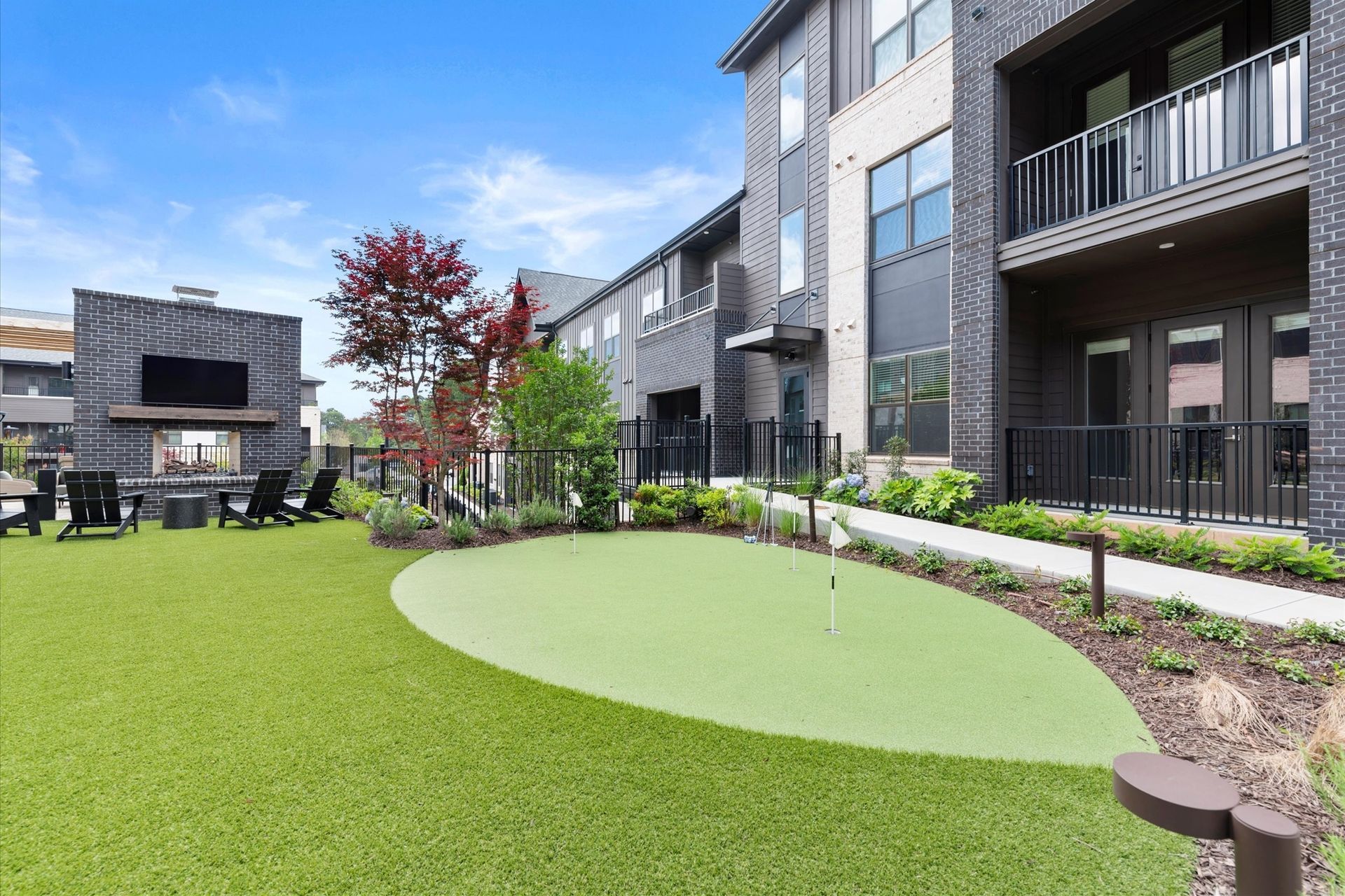 An outdoor recreation area with a putting green, fireplace, and apartment building.