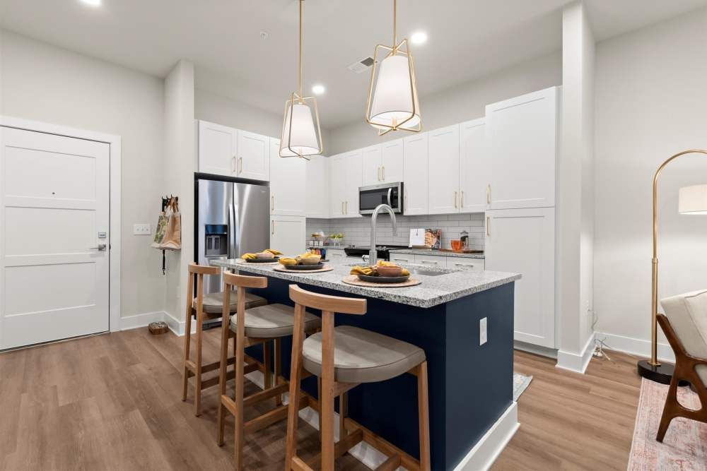 Modern kitchen with a blue island, granite countertops, and three bar stools. Stainless steel appliances and white cabinets.