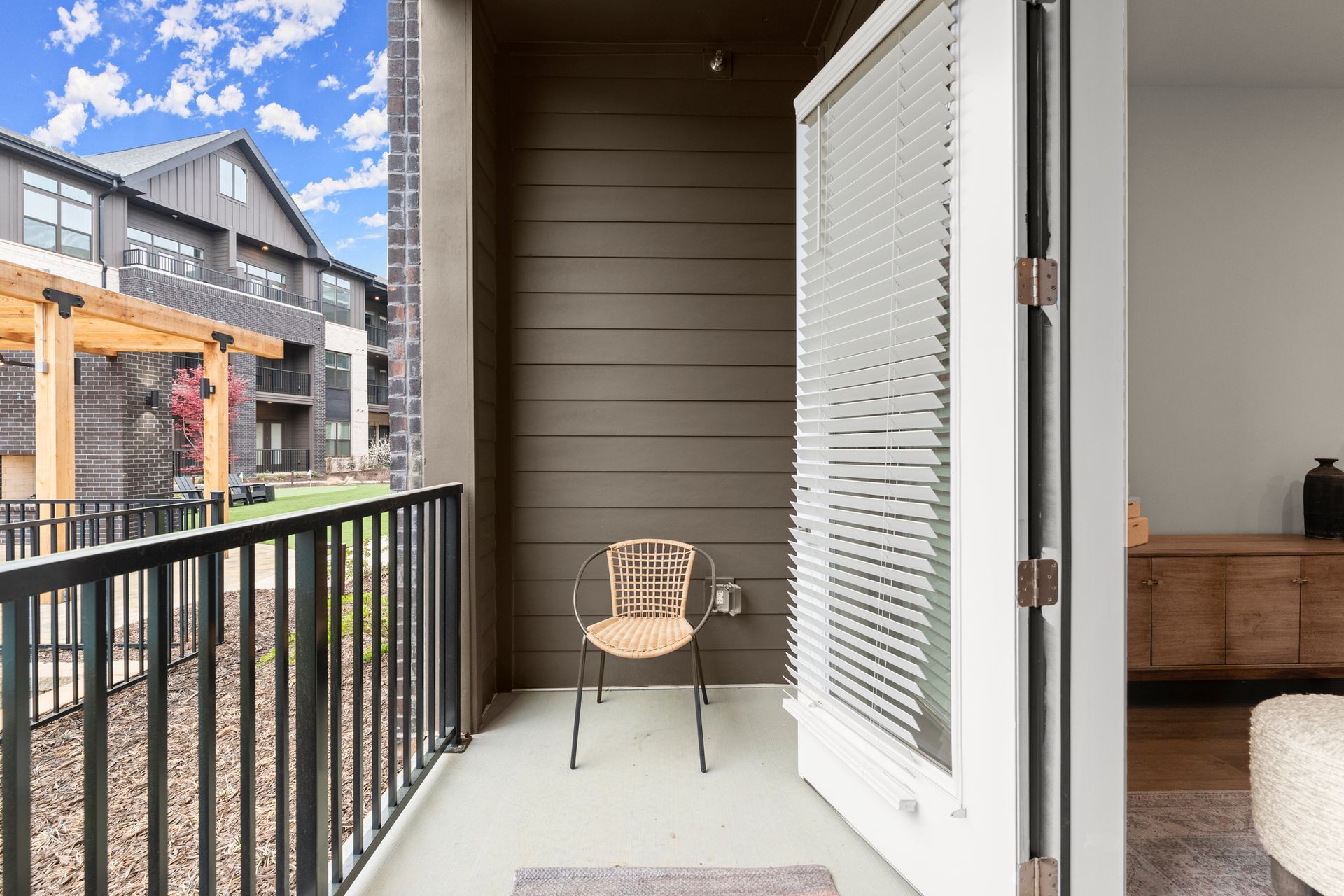 Balcony with a chair, open door to interior with wooden cabinet. Apartment complex in the background.