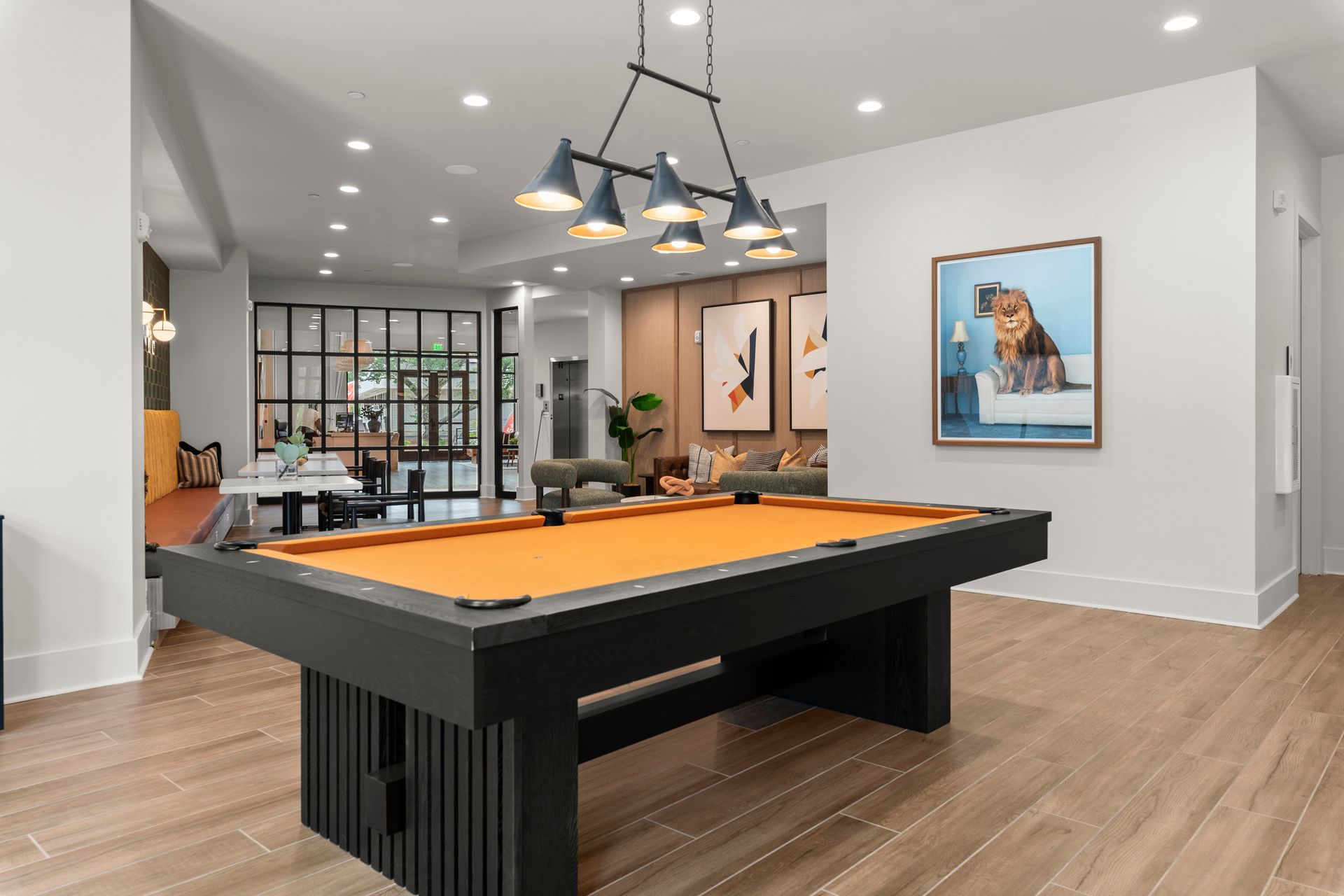Pool table with orange felt in a bright room with art and overhead lighting.