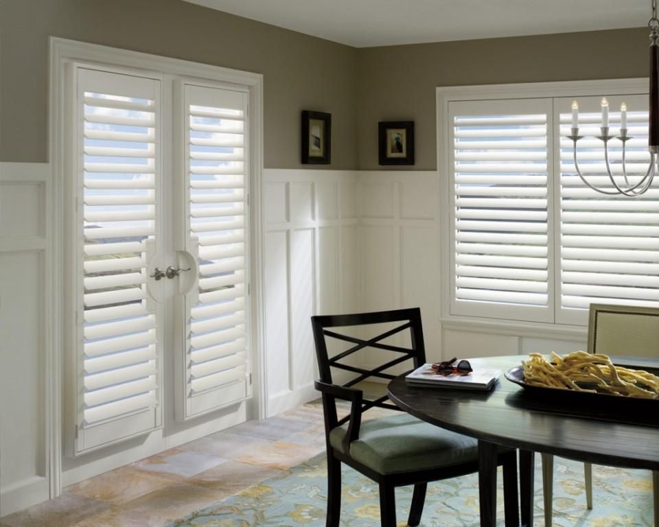 A dining room with a table and chairs and shutters on the windows.