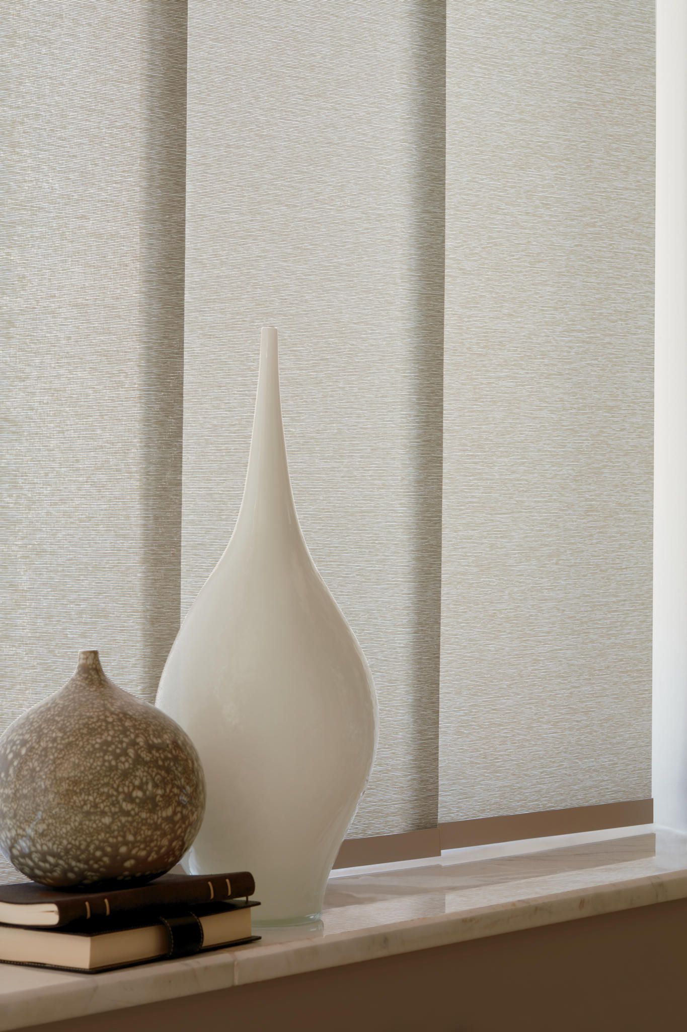 A white vase is sitting on a window sill next to a stack of books.