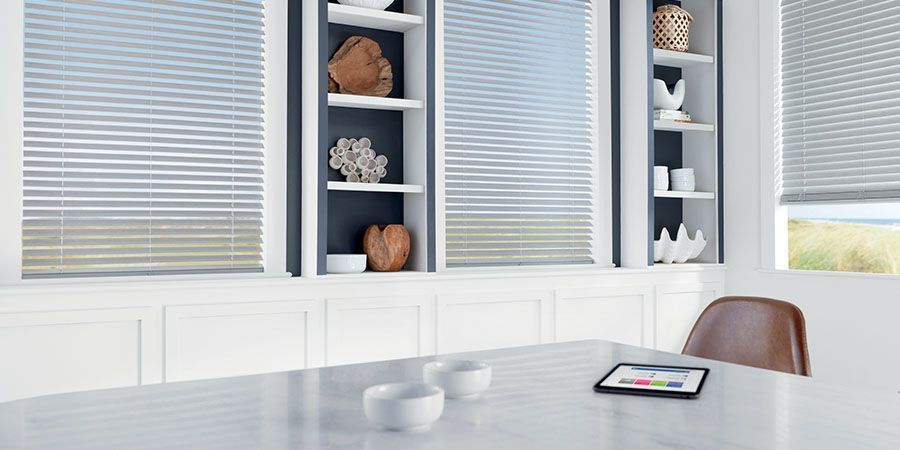 A dining room with a table , chairs , shelves and blinds.