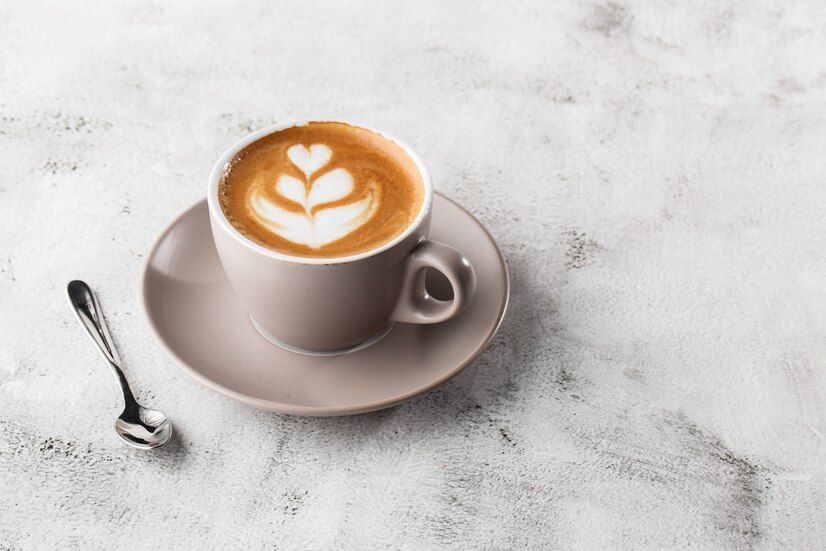 A cup of cappuccino with latte art and a spoon on a saucer on a table.