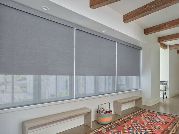 A room with a rug , benches , and roller shades on the windows.