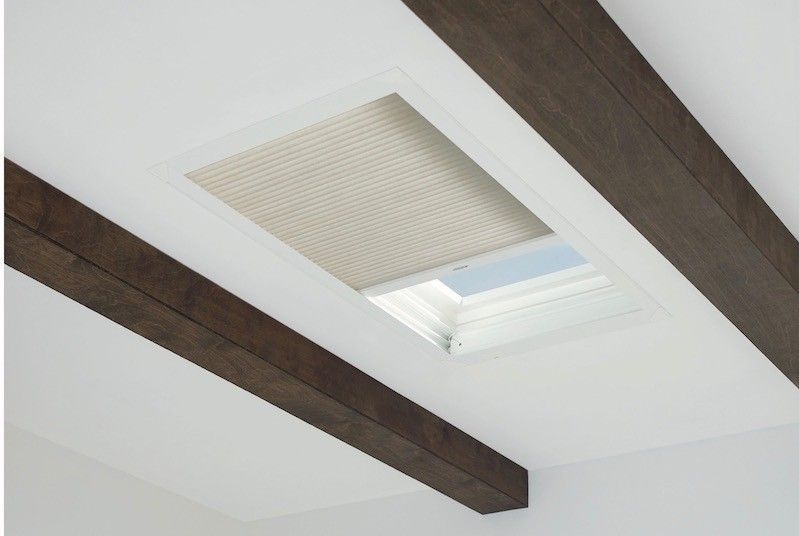 A skylight with a blind on it and wooden beams on the ceiling