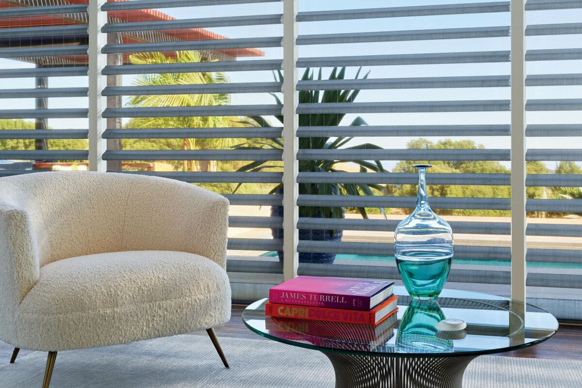 A chair and a table in front of a window with blinds.