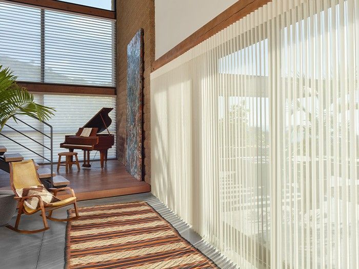 A living room with a piano , chair , rug and blinds.