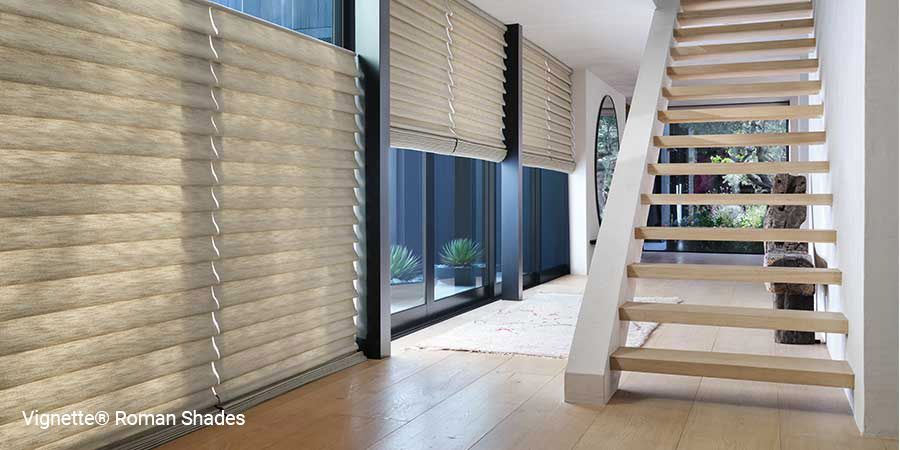 A hallway with a staircase and roman shades on the windows.