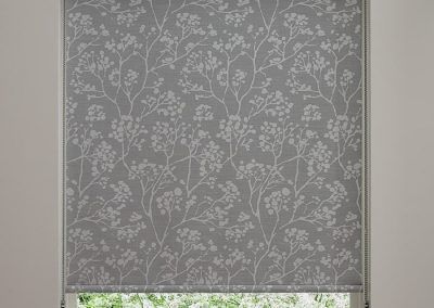 A gray roller blind with white flowers on it is hanging on a window.