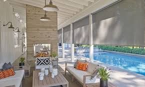 A screened in porch with a couch , table , chairs and a swimming pool.