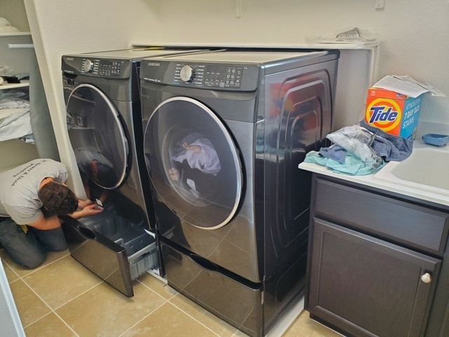 A man is working on a washer and dryer in a laundry room.