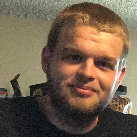 A man with a beard is wearing a black shirt and smiling for the camera.