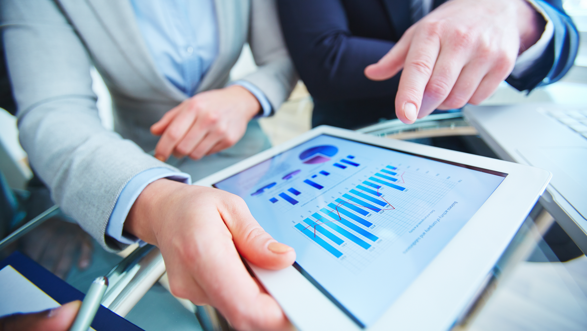 A man and a woman are looking at a tablet with a graph on it.