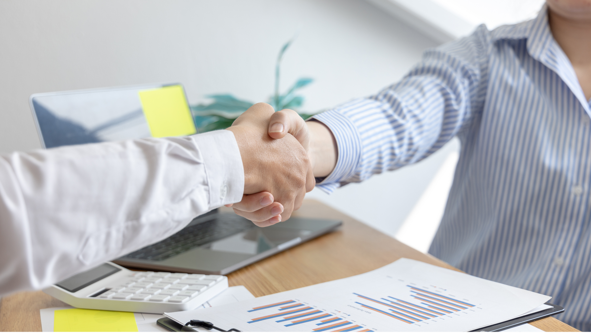 A man and a woman are shaking hands over a table.