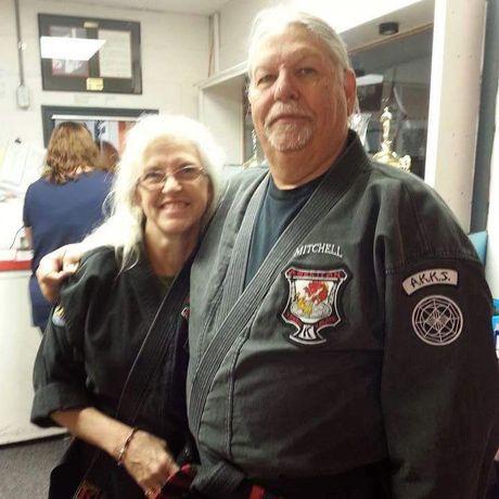 A man and woman are posing for a picture and the man has a patch on his arm that says a.m.k.s.