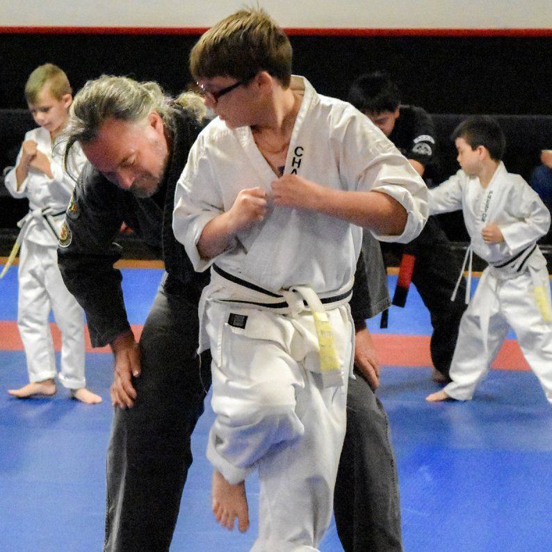 A man is helping a young boy in a taekwondo class