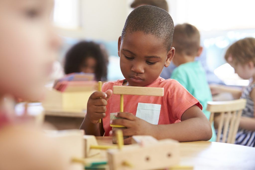 A young boy is playing with a wooden toy in a classroom.