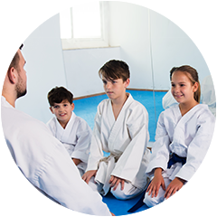 A group of children are sitting on the floor in a circle while a man talks to them.