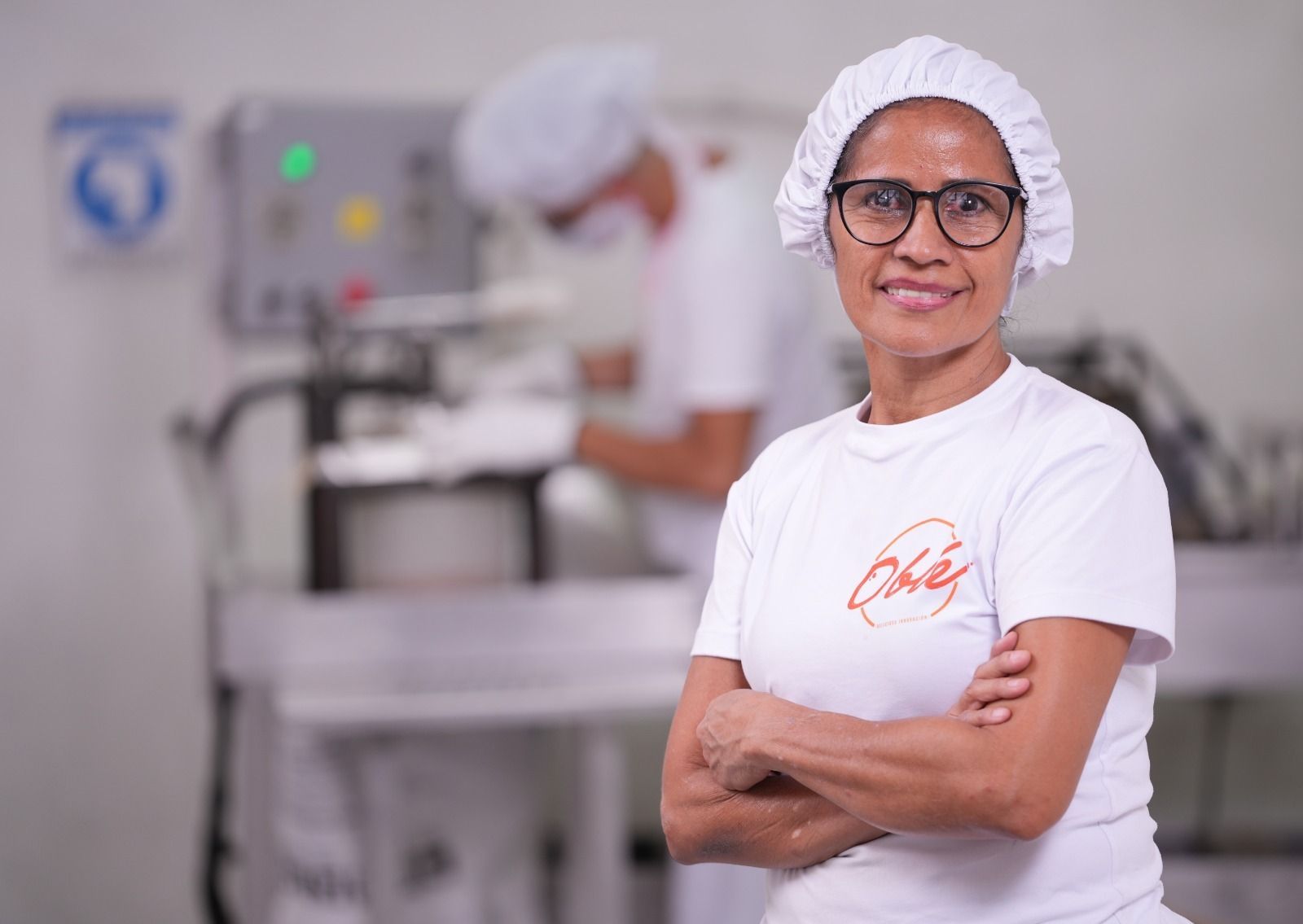 Una mujer que lleva un sombrero blanco y gafas está parada en una cocina con los brazos cruzados.