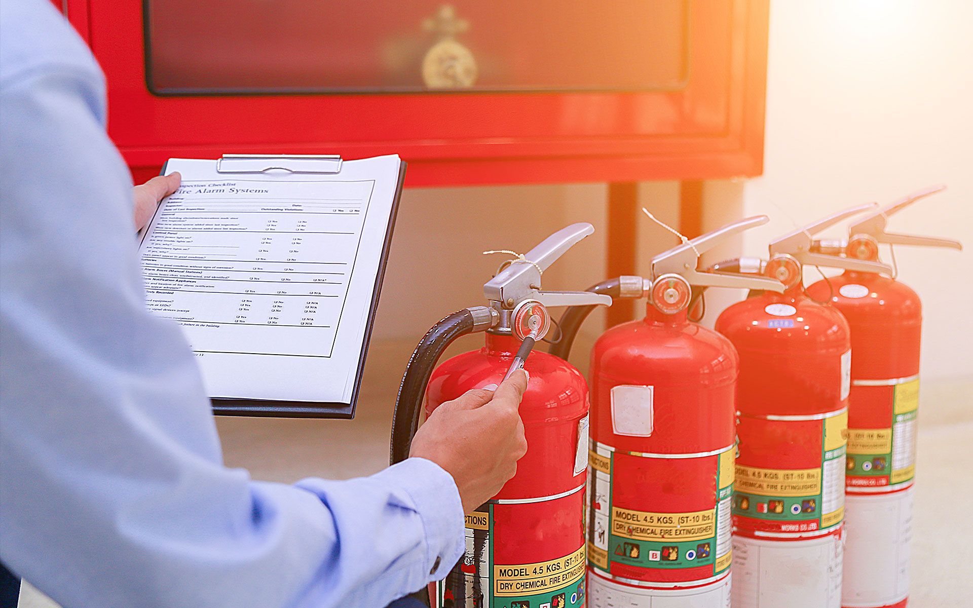 A man is holding a fire extinguisher in front of a row of fire extinguishers.
