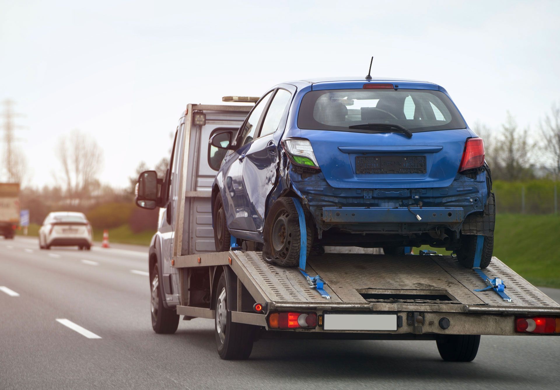 A blue car is being towed by a tow truck on a highway.