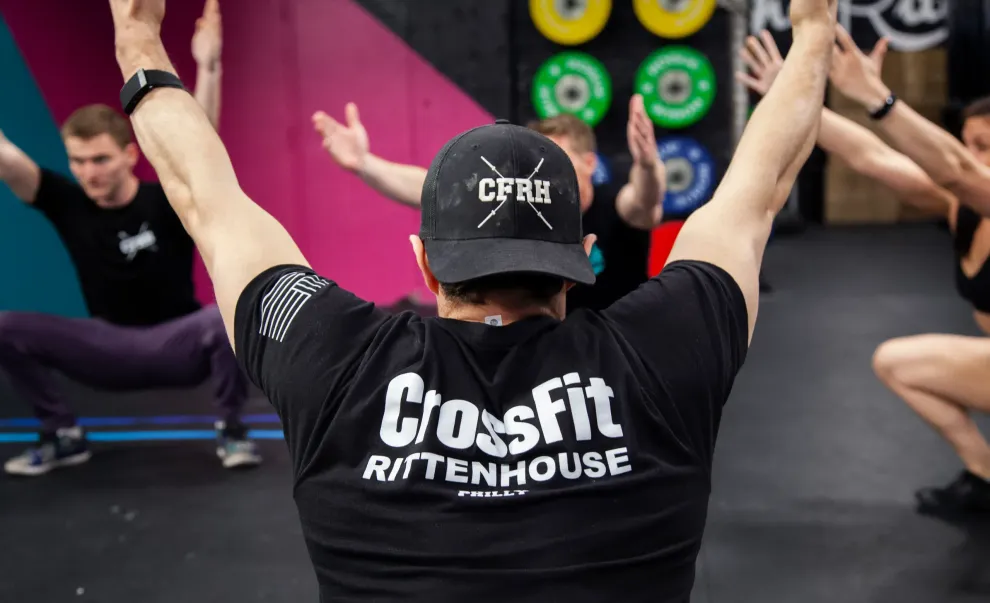 A man wearing a crossfit shirt is standing in front of a group of people doing squats.