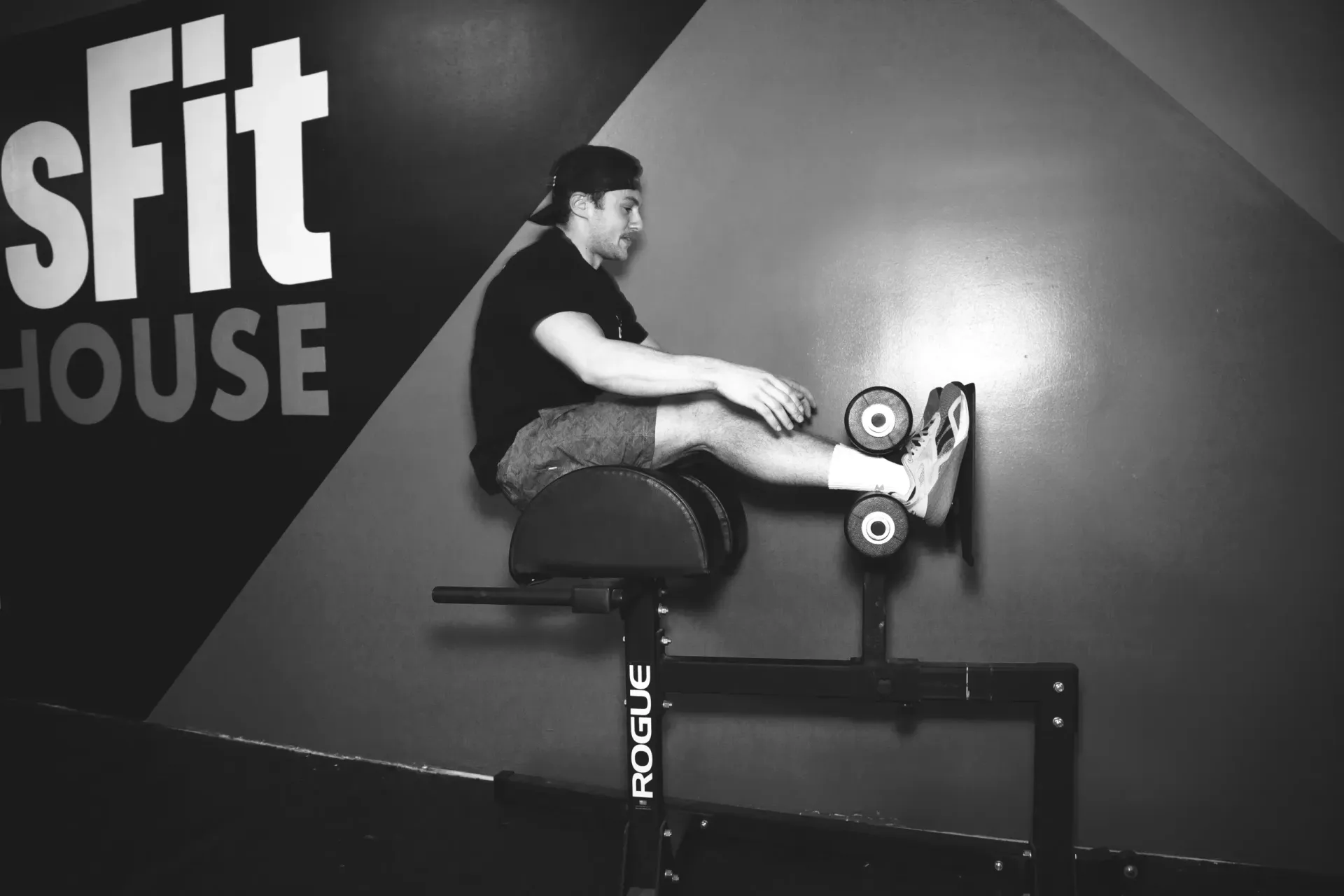 A man is squatting on a bench in front of a sign that says sfit house