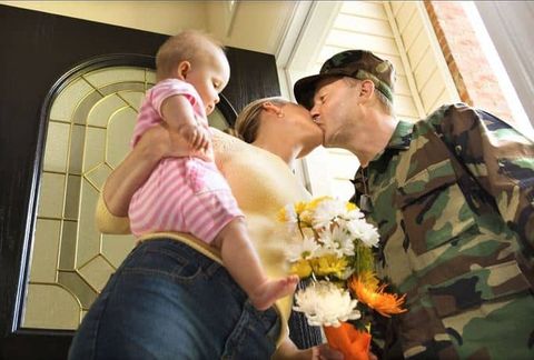 A wife kissing her husband who is just coming home from the military
